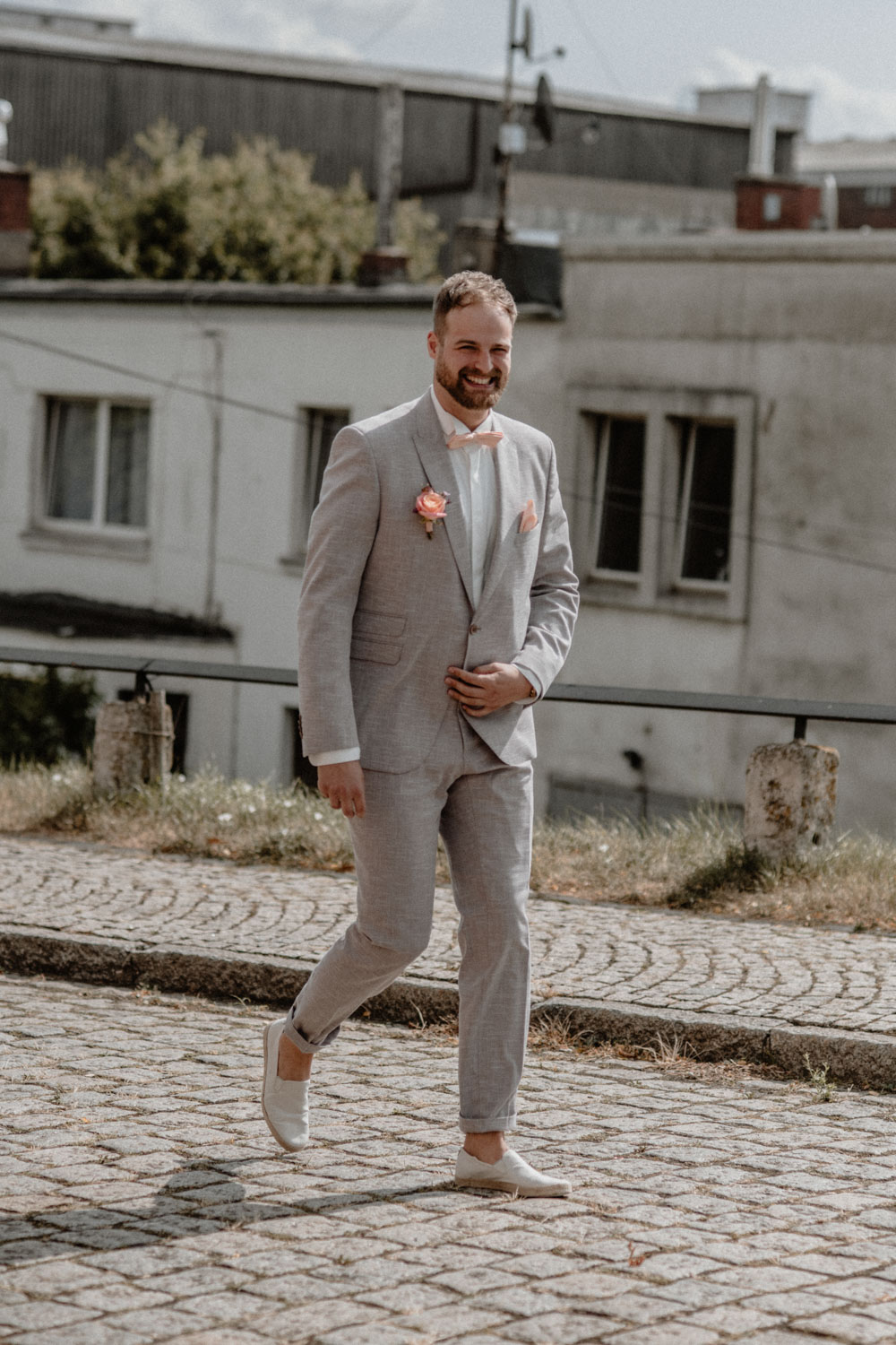 Bräutigam in hellem Anzug auf Kopfsteinpflaster