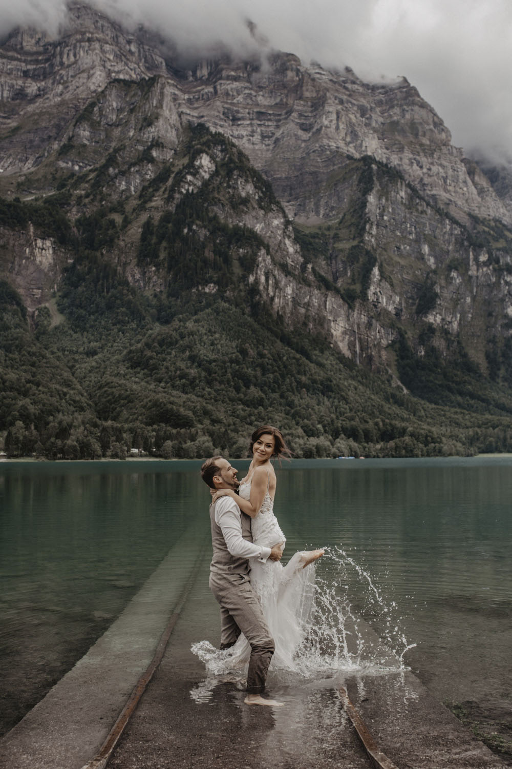Bräutigam trägt Braut lachend durchs Wasser