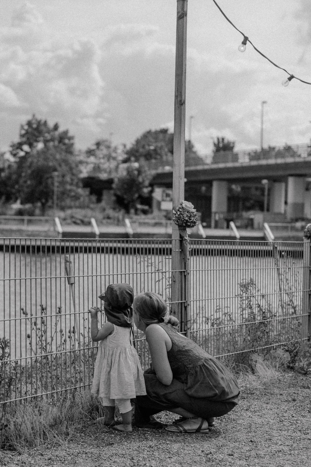 Frau und Kind blicken durch Zaun am Wasser