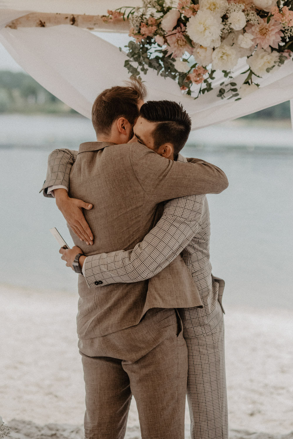 Bräutigam umarmt Trauzeugen unter dem Traubogen