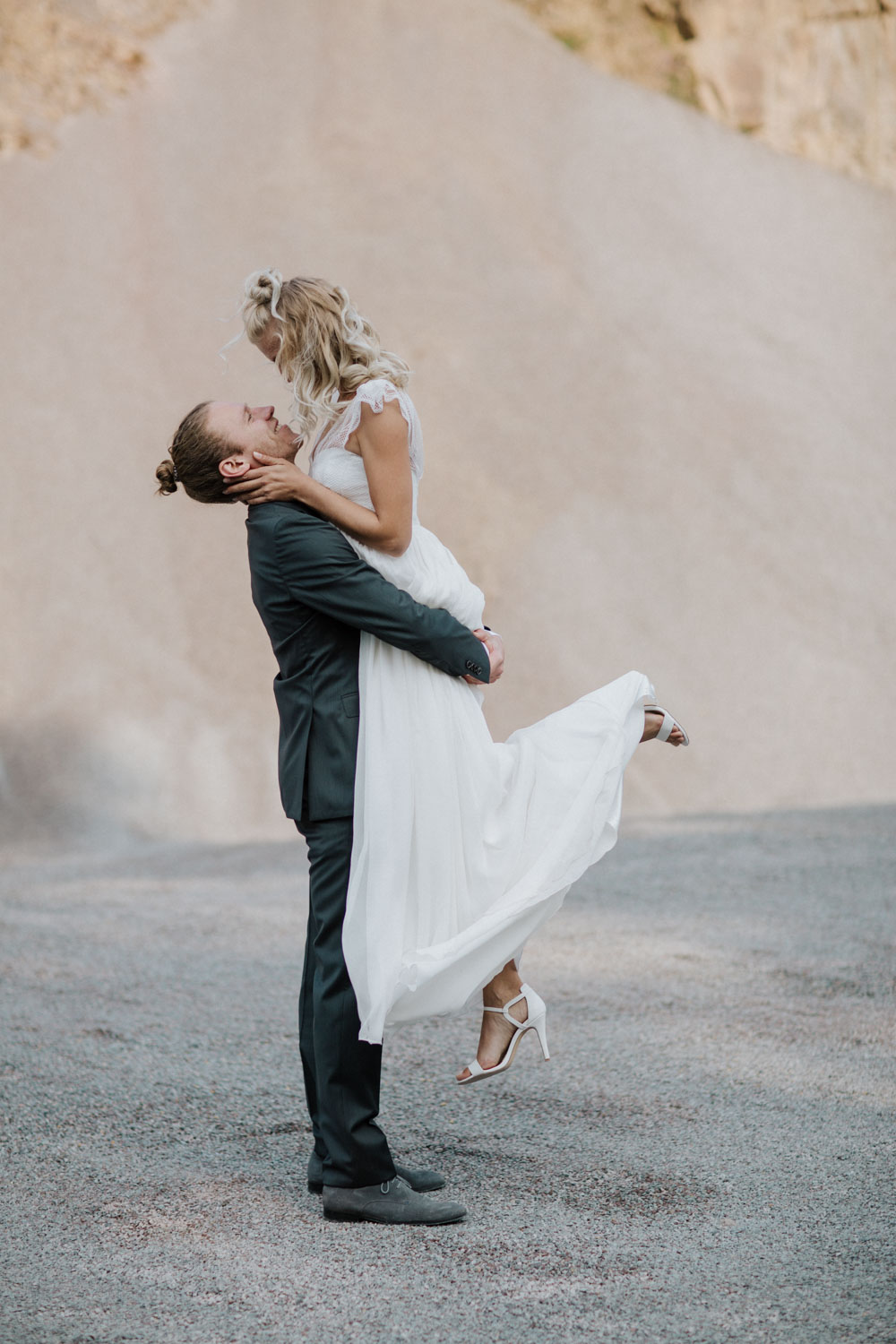 Bräutigam hebt lachende Braut vor hellem Hintergrund