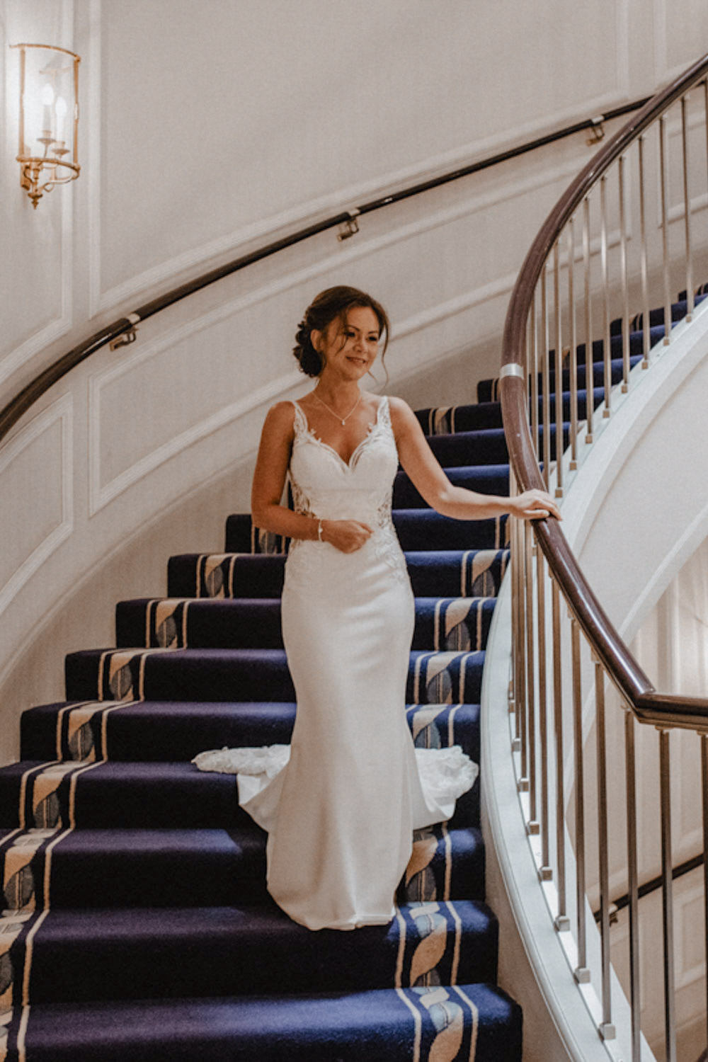 Braut steigt lächelnd die Hoteltreppe im Hochzeitskleid hinab