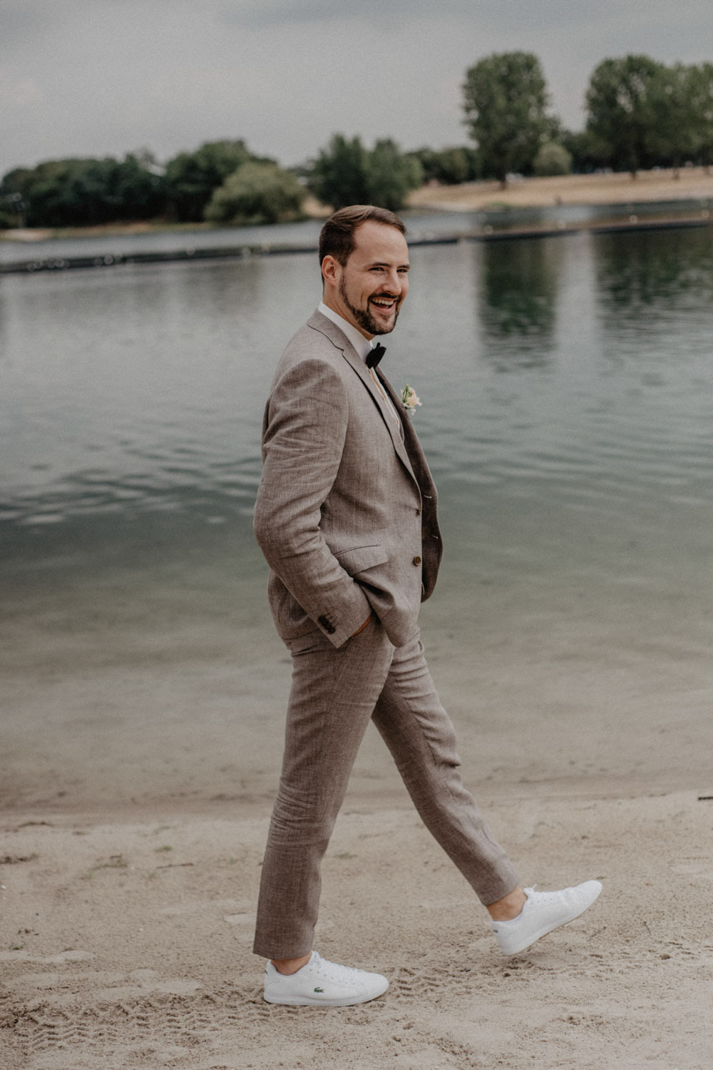 Bräutigam läuft lächelnd am Seeufer entlang