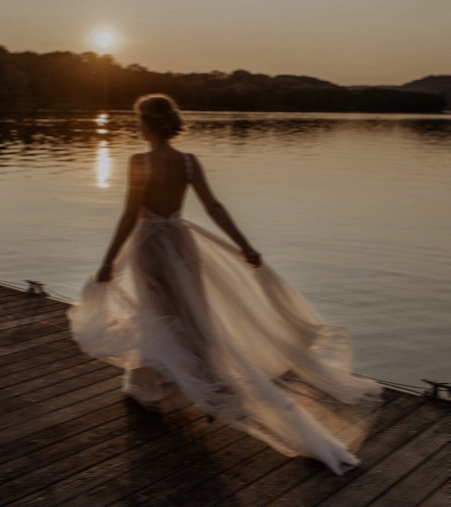 Braut läuft im Sonnenuntergang über einen Steg am See in Essen