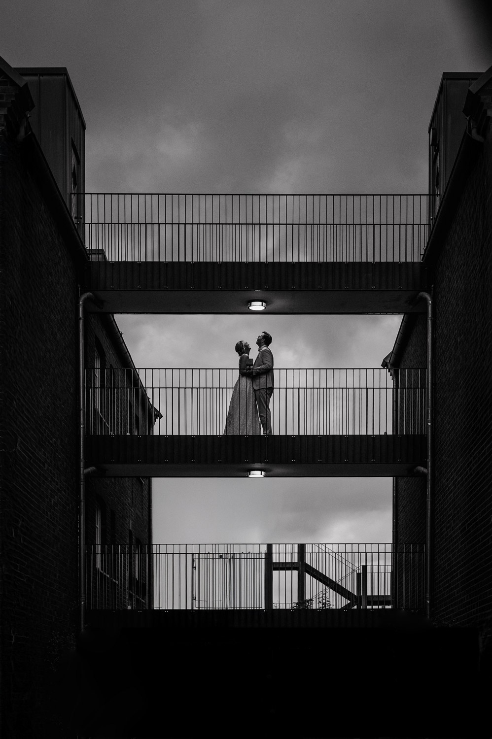 Brautpaar steht auf Brücke zwischen Backsteingebäuden