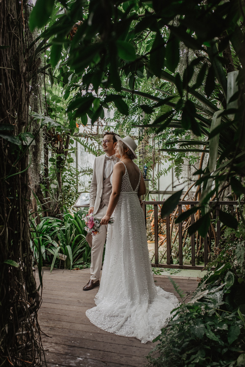 Brautpaar steht umgeben von tropischem Grün im Gewächshaus