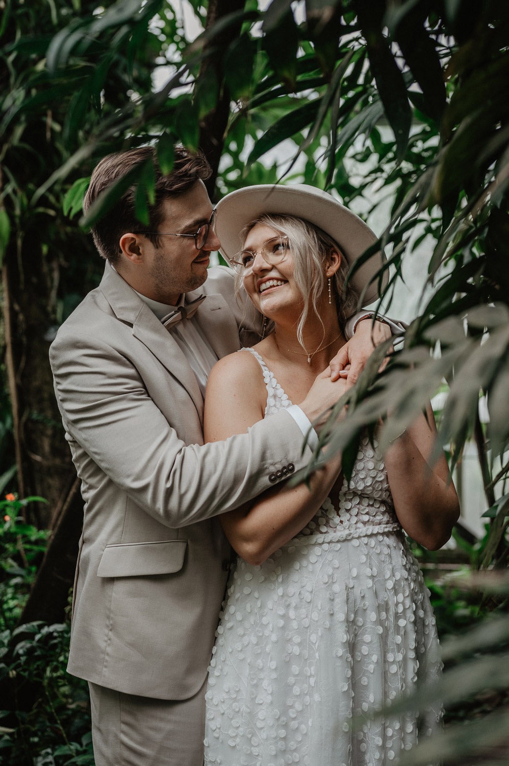 Bräutigam umarmt Braut zwischen tropischen Pflanzen