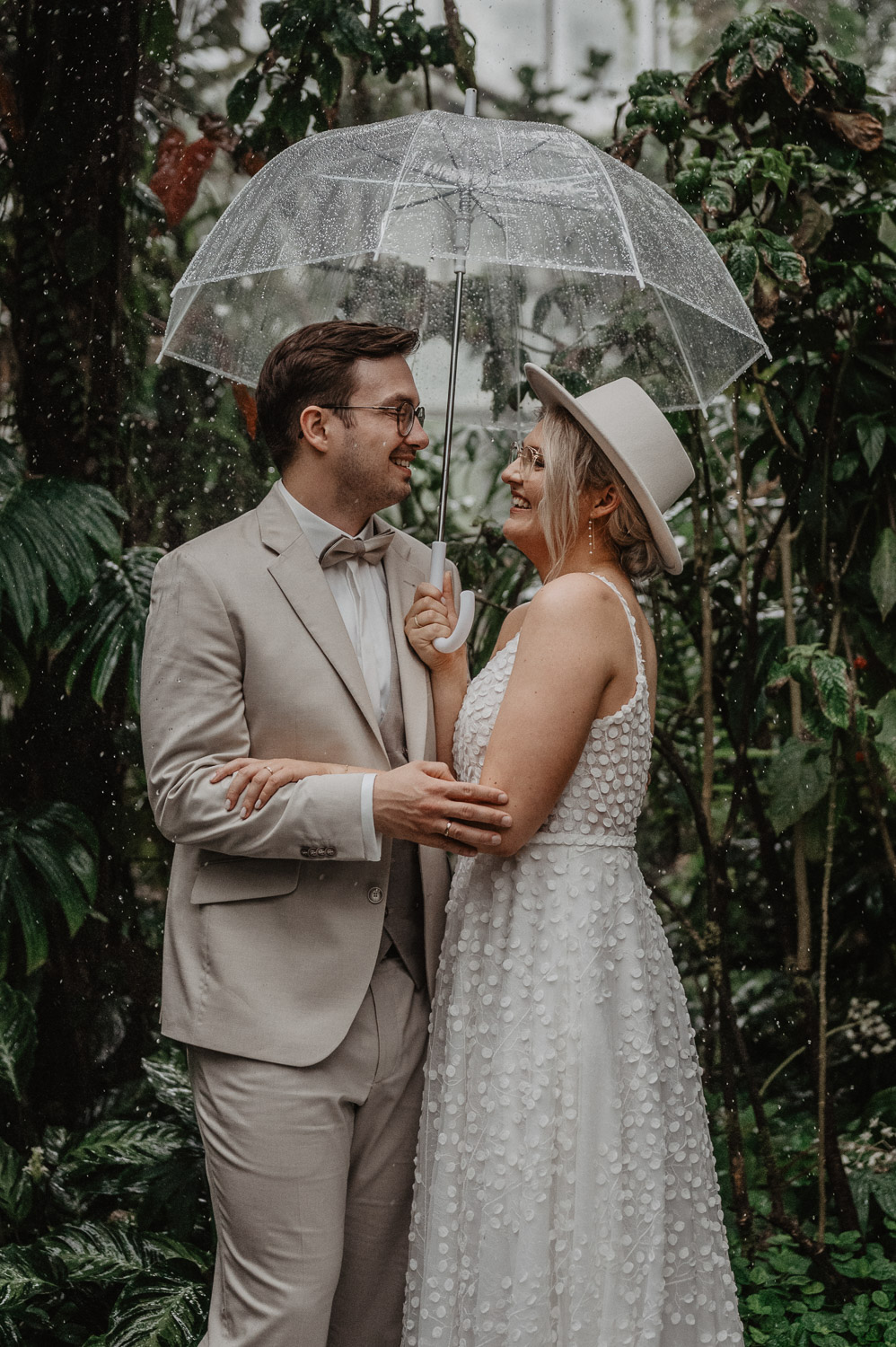 Brautpaar lacht unter durchsichtigem Regenschirm