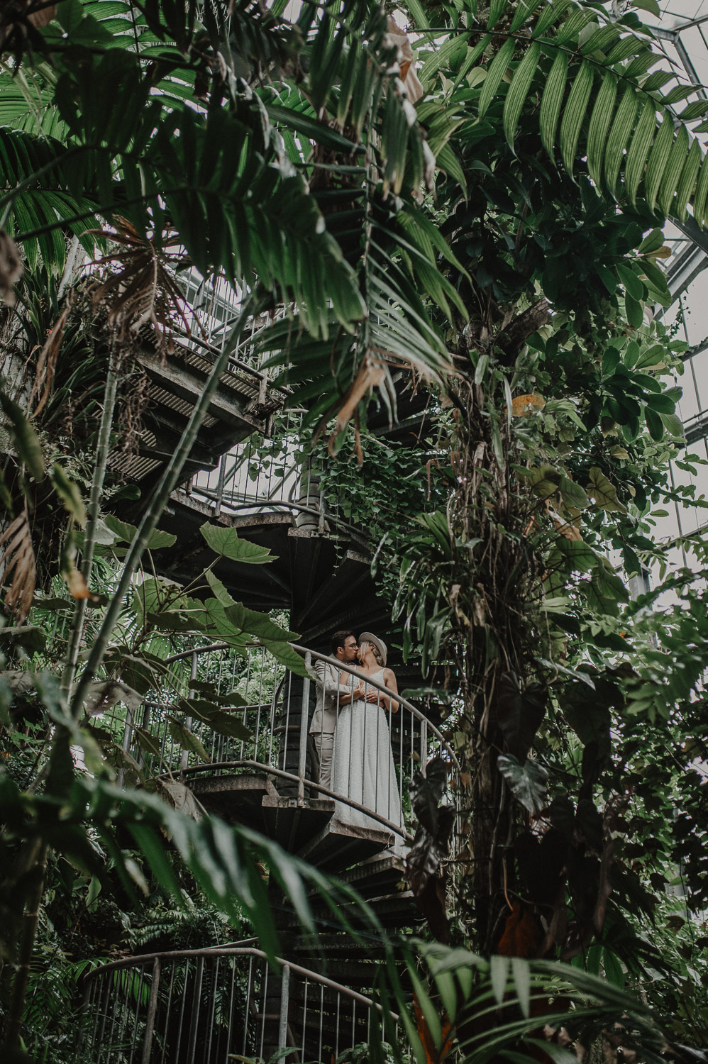 Brautpaar steht auf Wendeltreppe im Tropenhaus