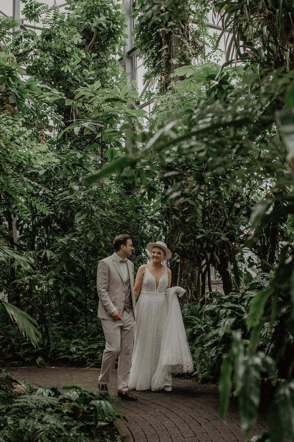 Braut und Bräutigam lachen im tropischen Gewächshaus