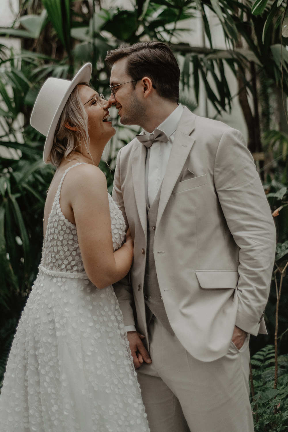 Braut und Bräutigam lachen sich im Gewächshaus an