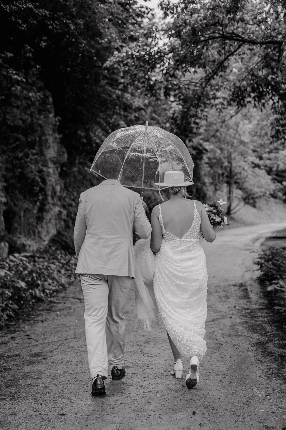 Brautpaar läuft mit durchsichtigem Regenschirm durch Waldweg