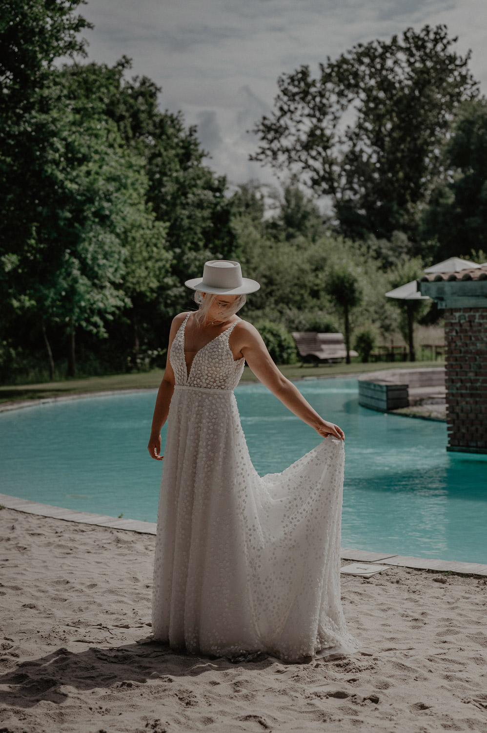 Braut mit Boho-Hut steht am Pool in Beverland
