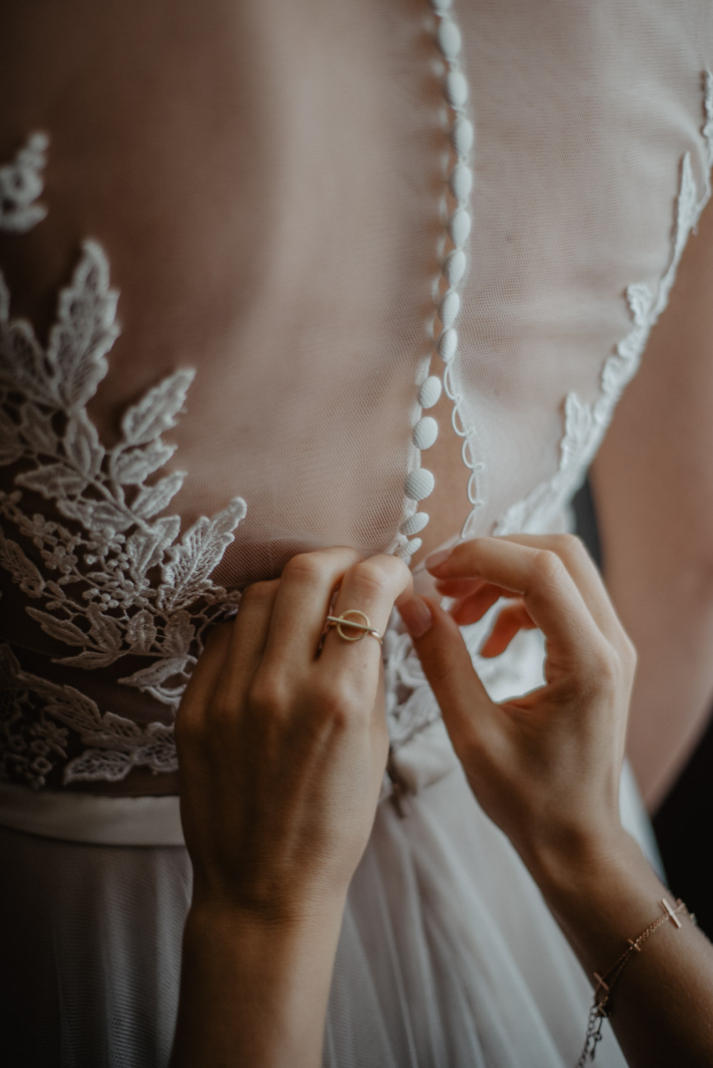 Detailaufnahme des Rückens der Braut beim Schließen des Hochzeitskleides.
