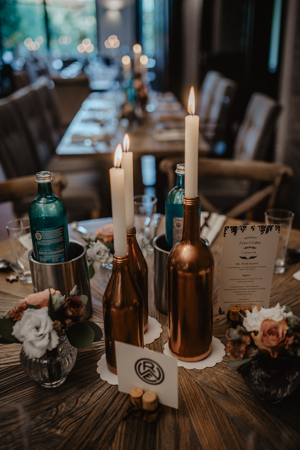 Kerzen in kupferfarbenen Flaschen als Tischdeko bei der Herbsthochzeit.