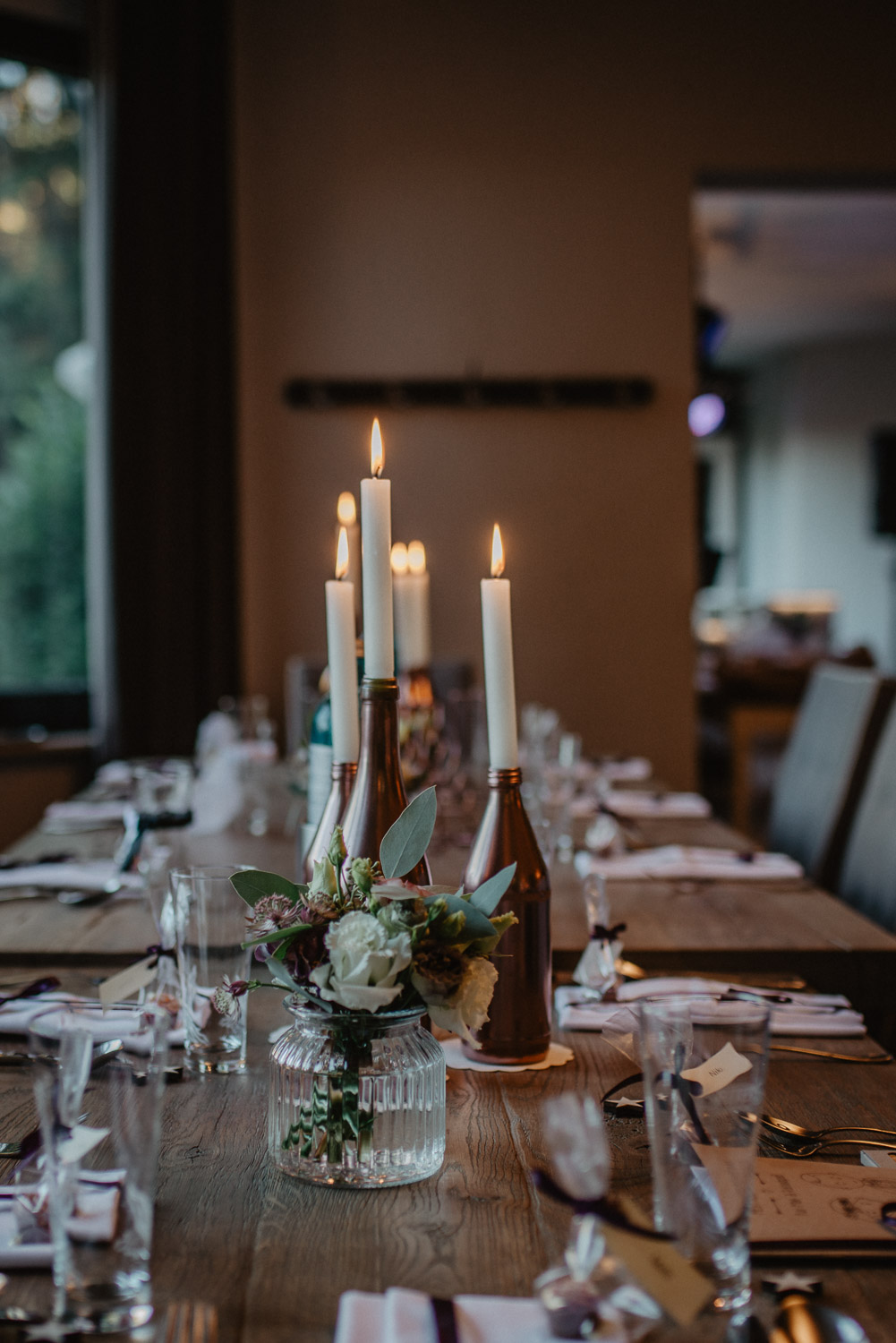 Tisch mit Kerzen, Menükarten und kleinen Blumengestecken.