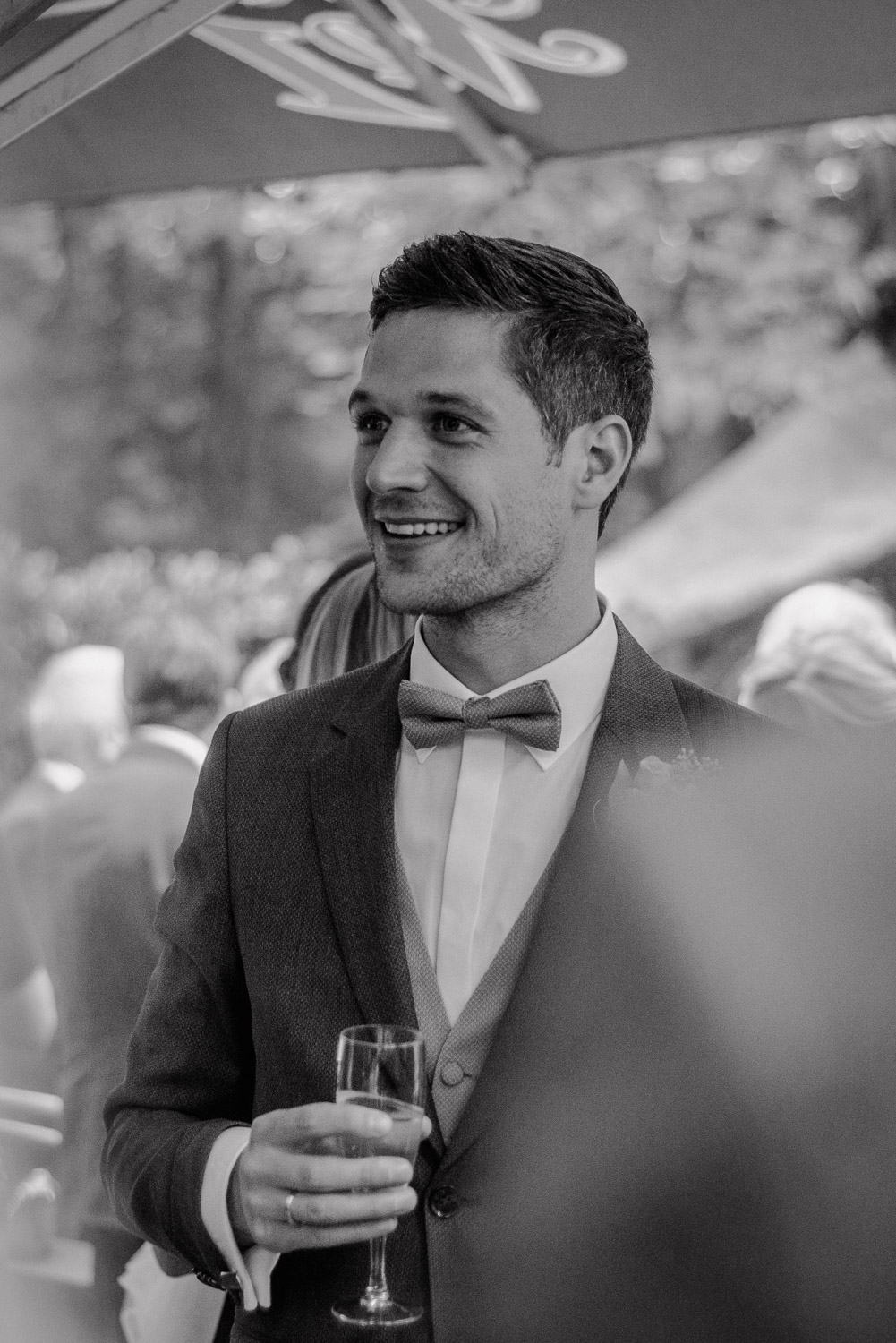 Bräutigam lacht entspannt mit Glas Sekt beim Empfang, Schwarz-Weiß.