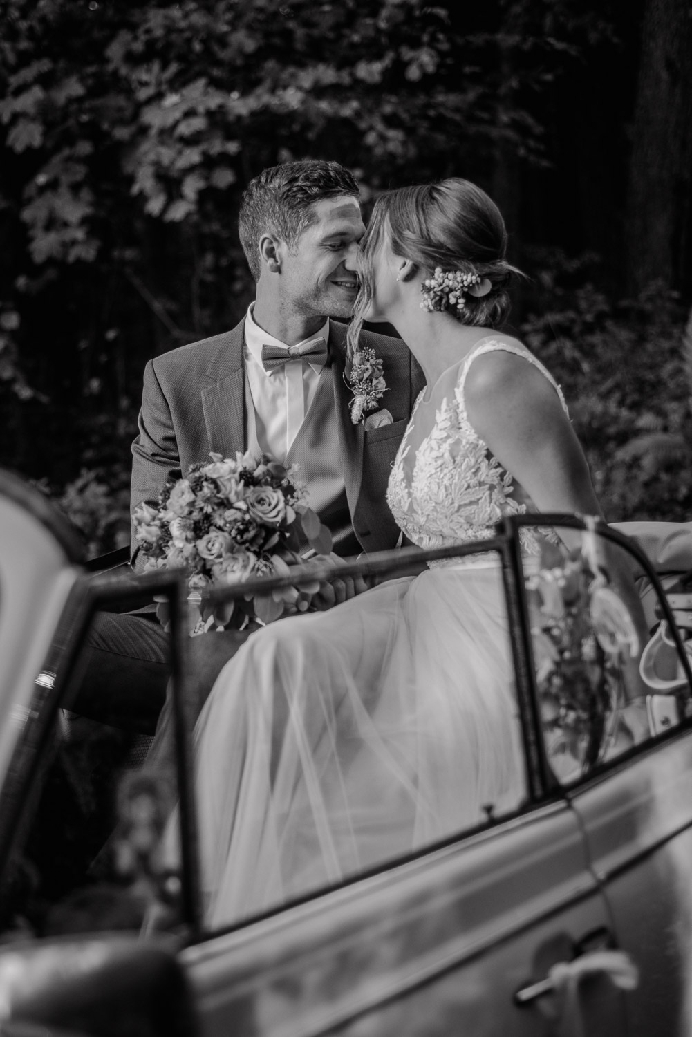 Braut und Bräutigam küssen sich im Cabrio, Schwarz-Weiß Aufnahme.