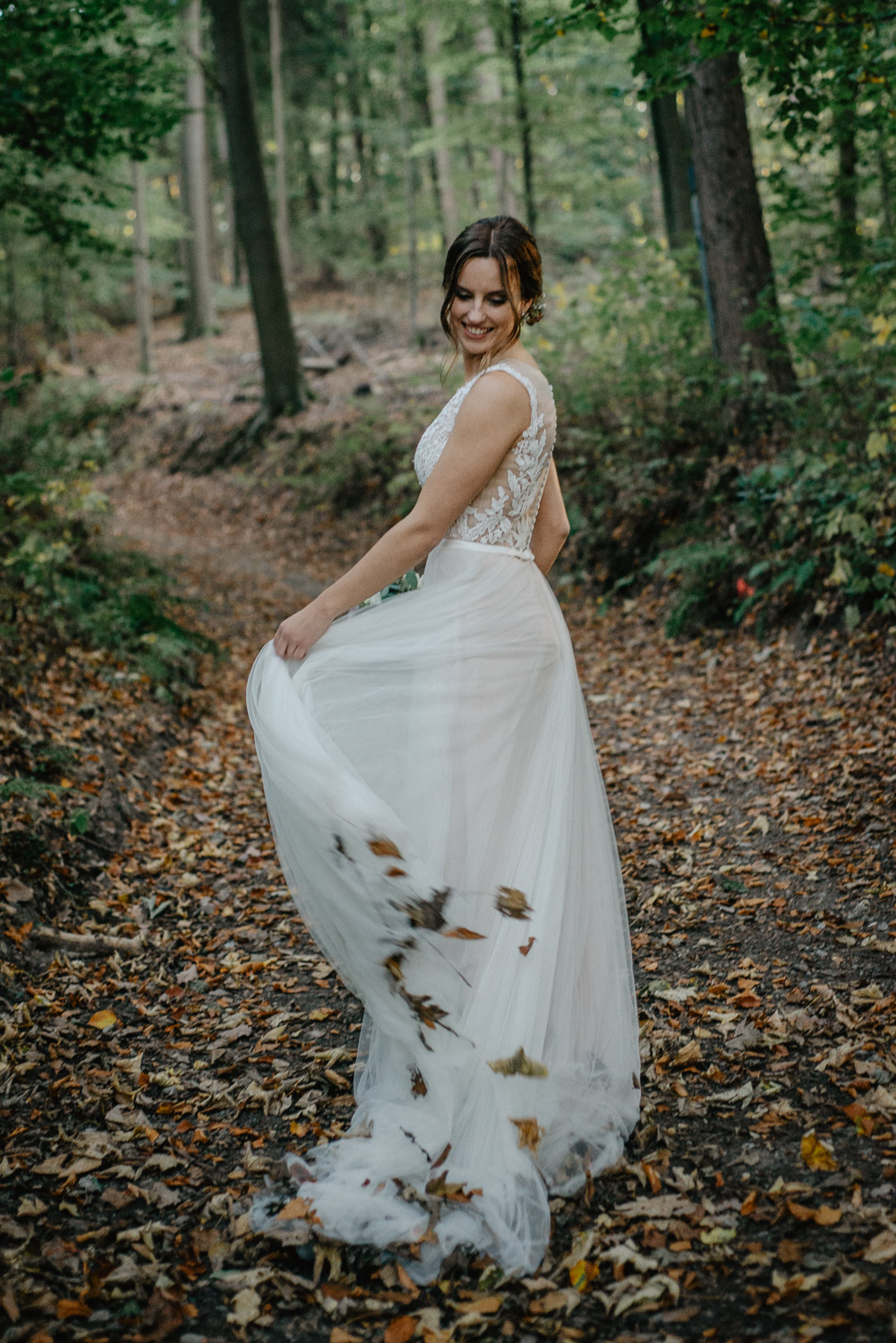 Braut wirbelt ihr Kleid voller Herbstblätter im Wald.