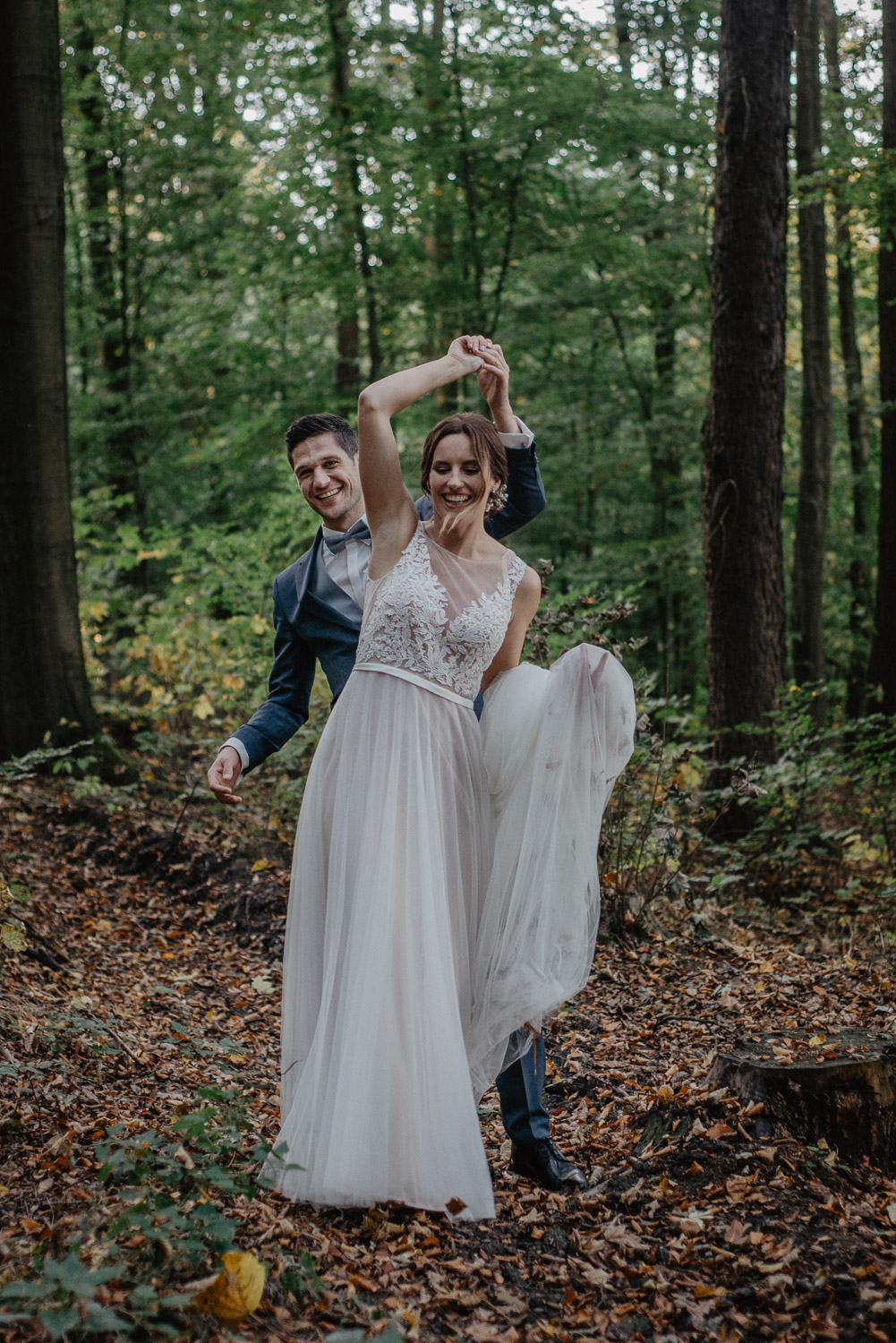 Brautpaar tanzt spielerisch im Wald bei der Herbsthochzeit.
