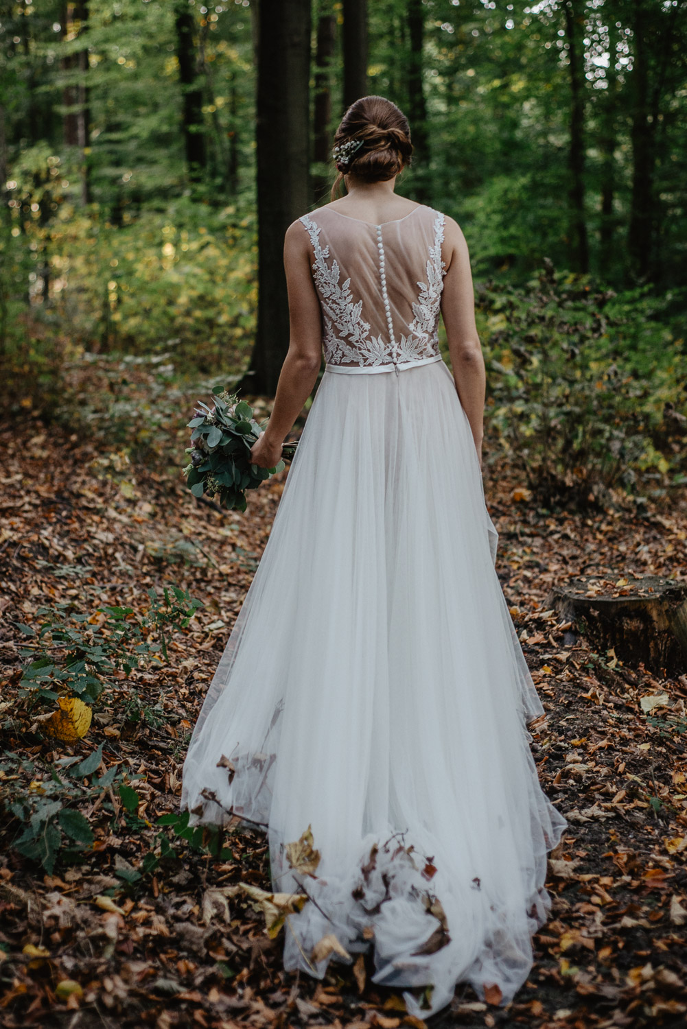 Rückenansicht der Braut mit langem Kleid auf Waldweg.