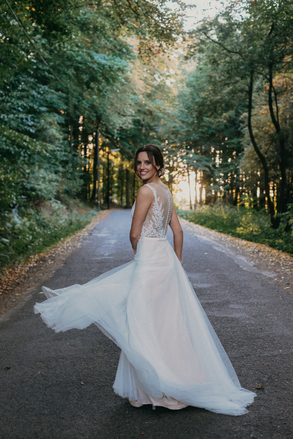 Braut dreht sich spielerisch auf einer Allee im Sonnenuntergang.