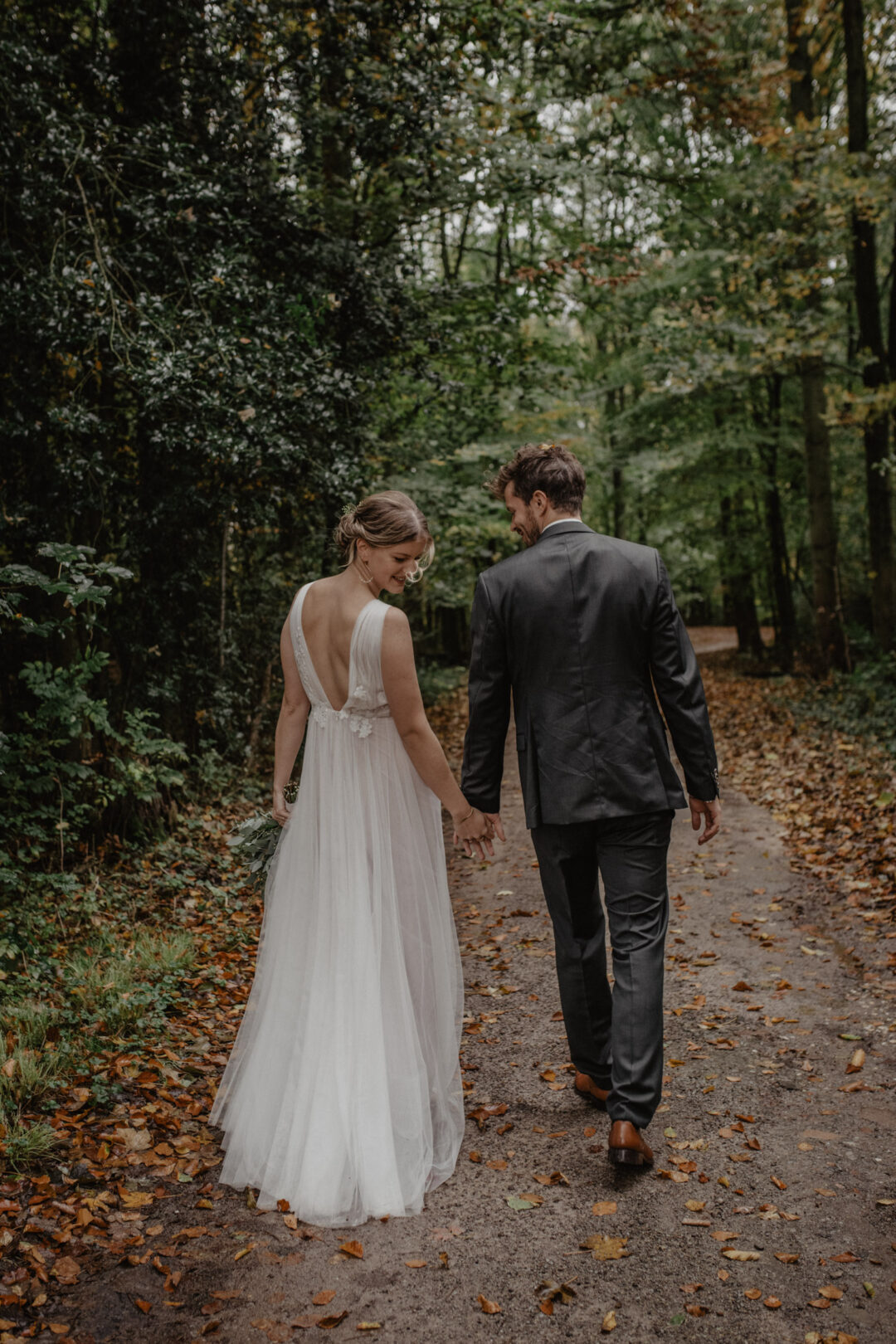 Braut und Bräutigam gehen Hand in Hand durch den Wald