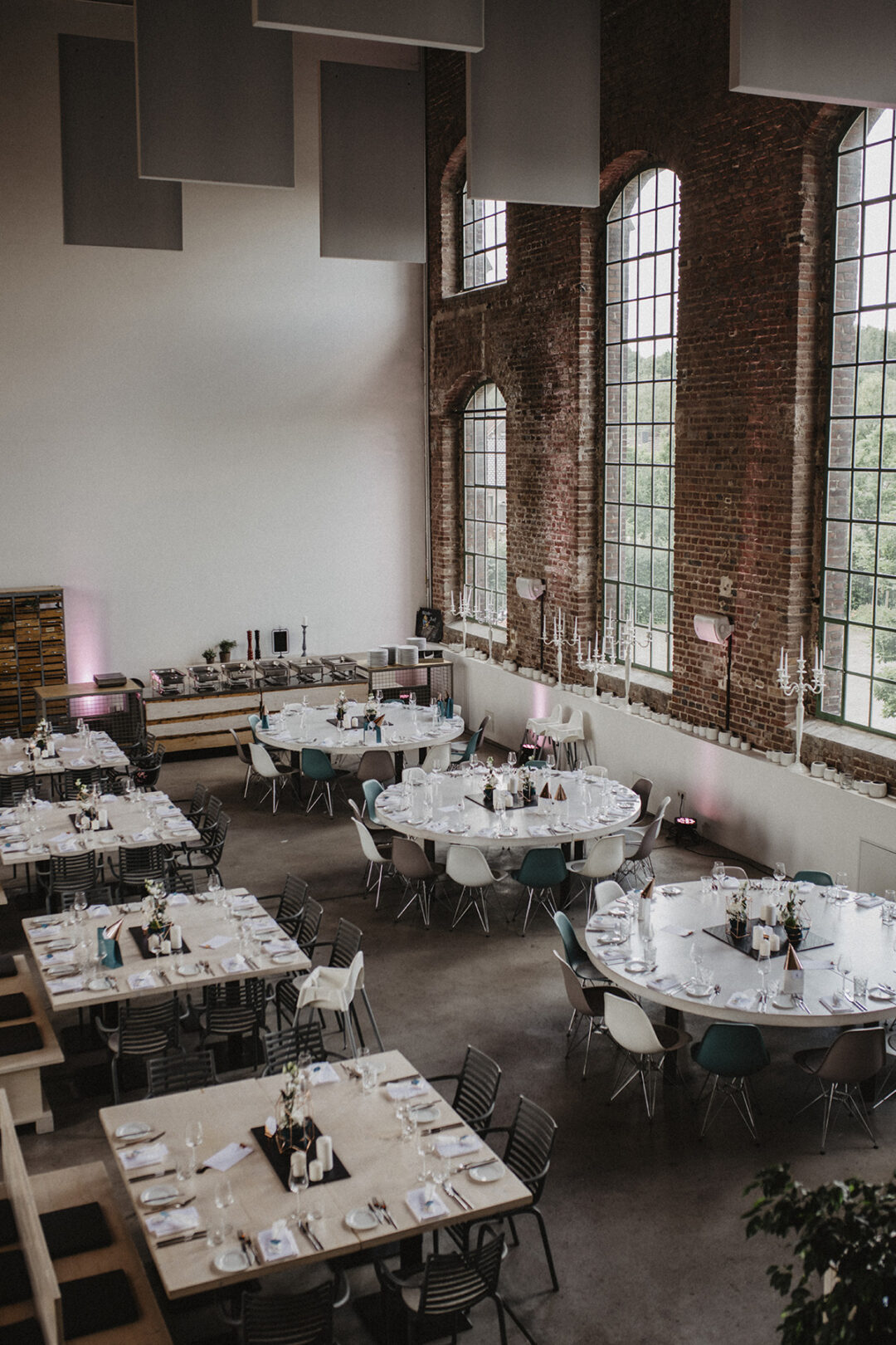 Festlich eingedeckte Tische im Industrieambiente mit Backstein und großen Fenstern