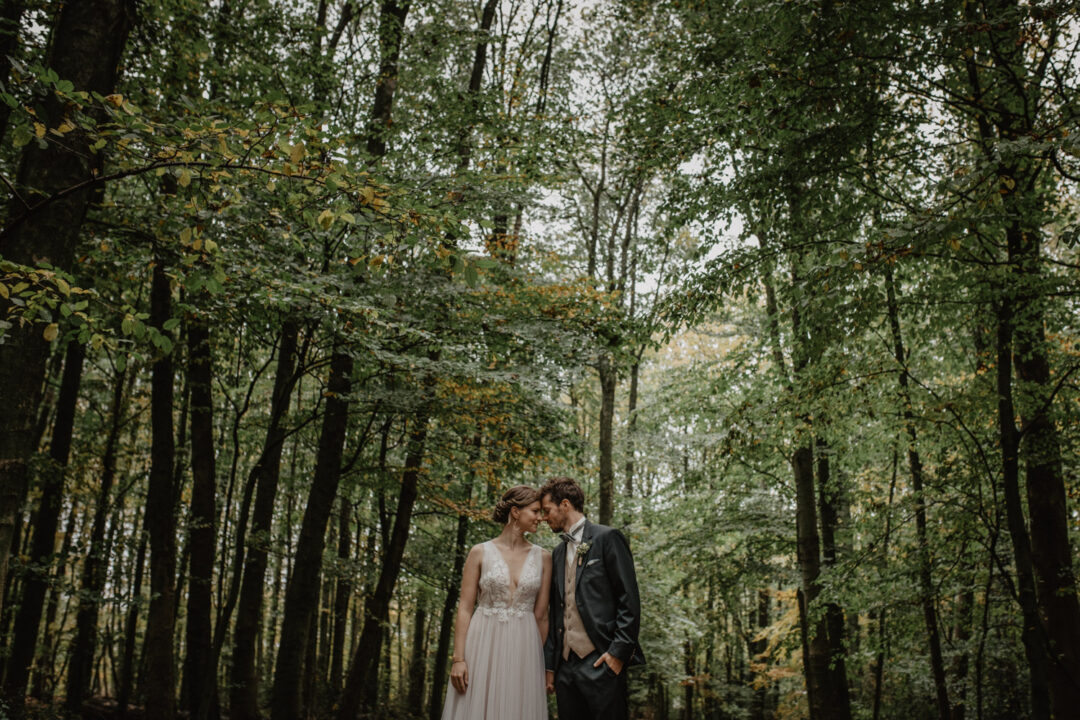 Brautpaar steht unter Bäumen bei First Look Shooting