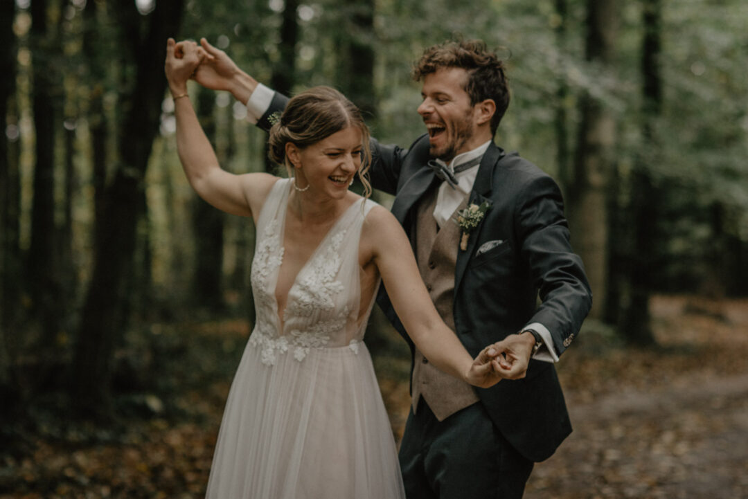 Braut und Bräutigam tanzen lachend im Wald