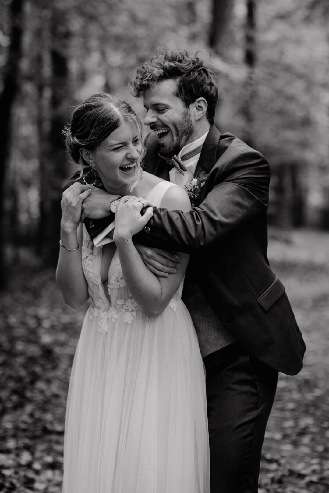 Brautpaar lacht ausgelassen beim Spaziergang durch den Wald