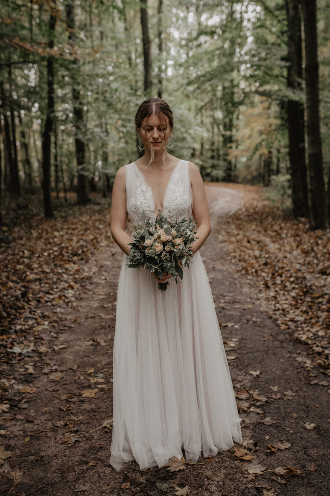 Braut steht mit Brautstrauß in der Hand im Wald