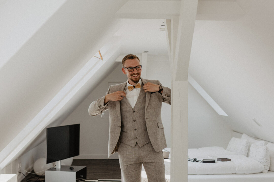 Bräutigam zieht seinen Anzug in heller Dachkammer an