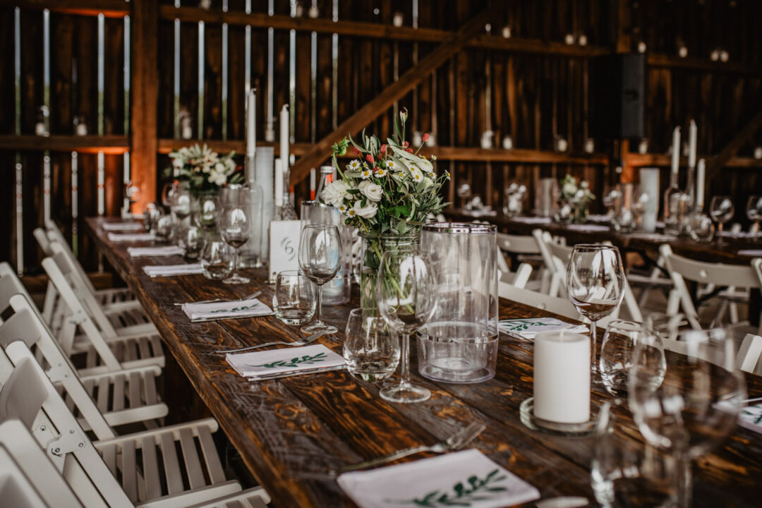 Holztische mit Blumenschmuck bei Scheunenhochzeit