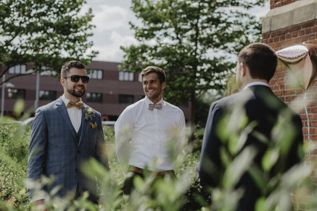 Gäste der Hochzeit in Anzügen und Sonnenbrille vor dem Gasthaus Stromberg