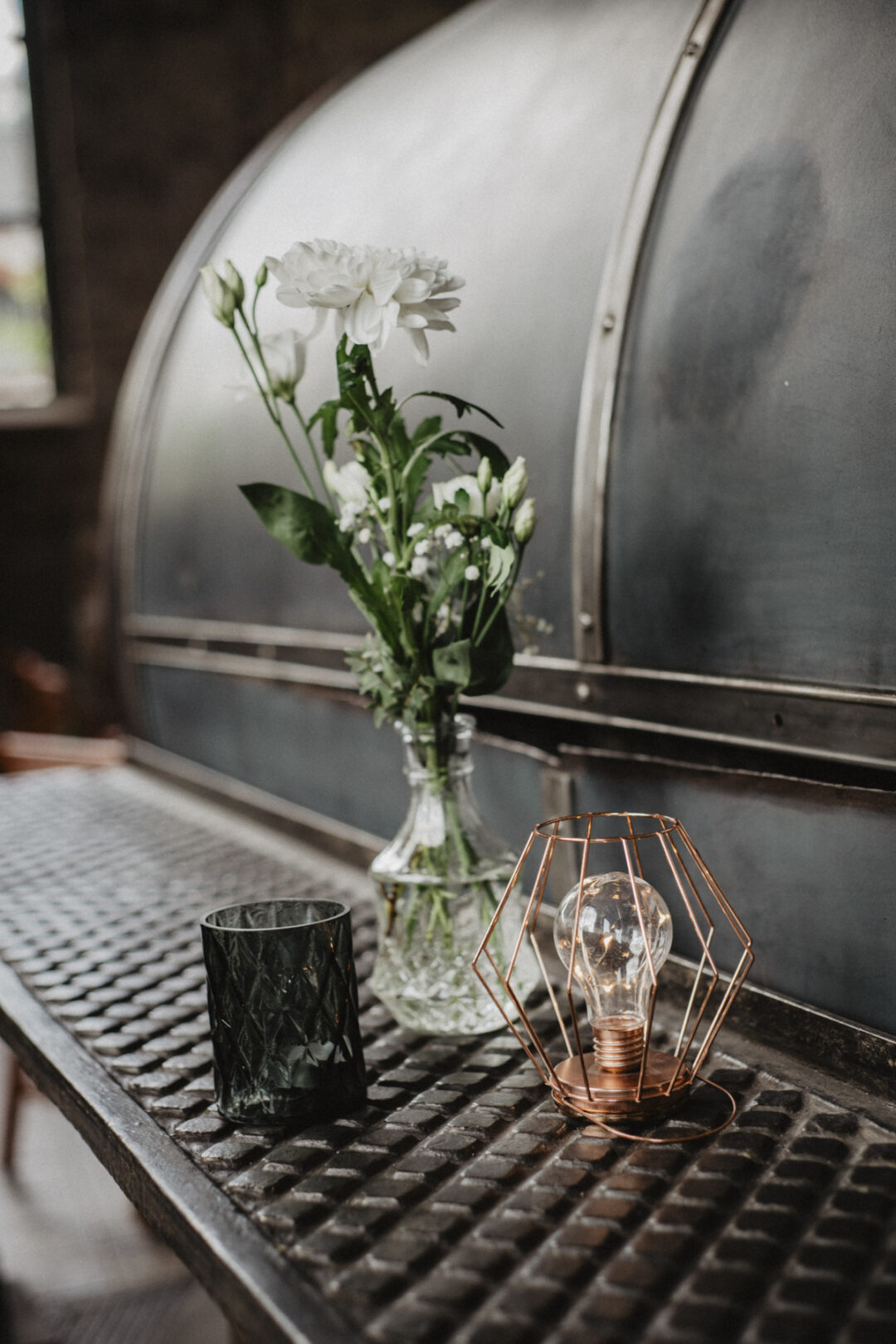Dekoration mit Blumen, Kerze und Glühbirne im Industrial-Stil
