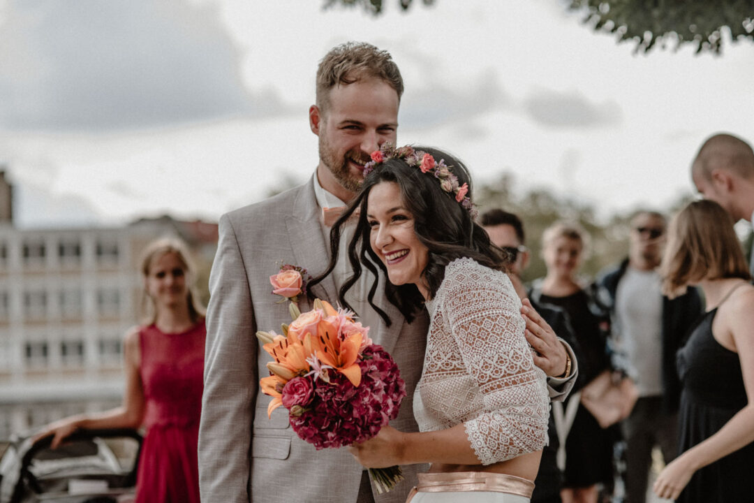 Brautpaar lacht glücklich mit Brautstrauß