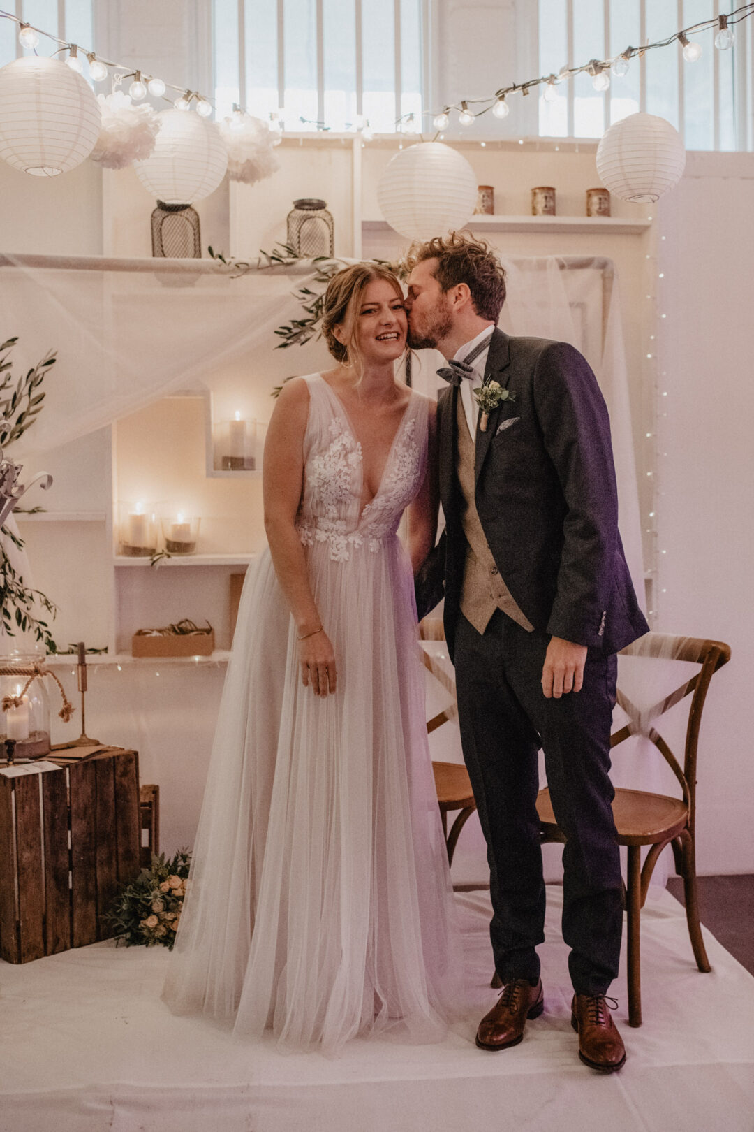 Brautpaar küsst sich unter geschmücktem Traubogen