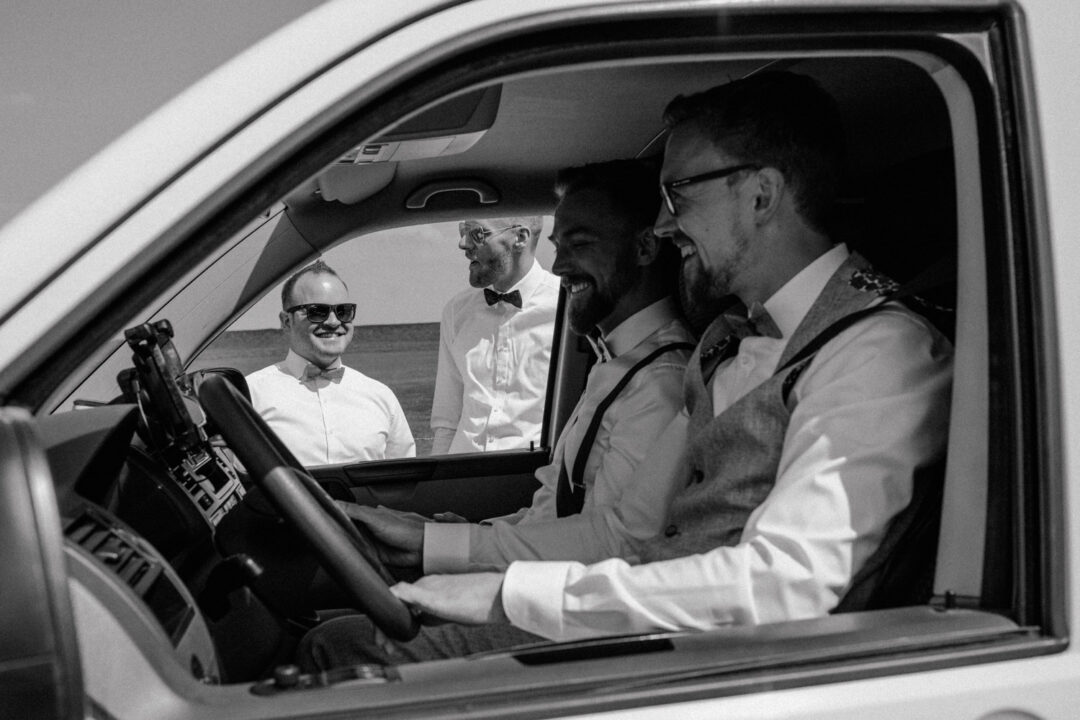 Bräutigam sitzt im Auto und lacht