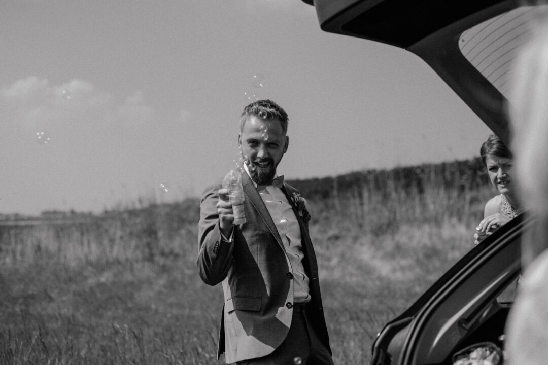 Bräutigam hält eine Sektflasche am Auto
