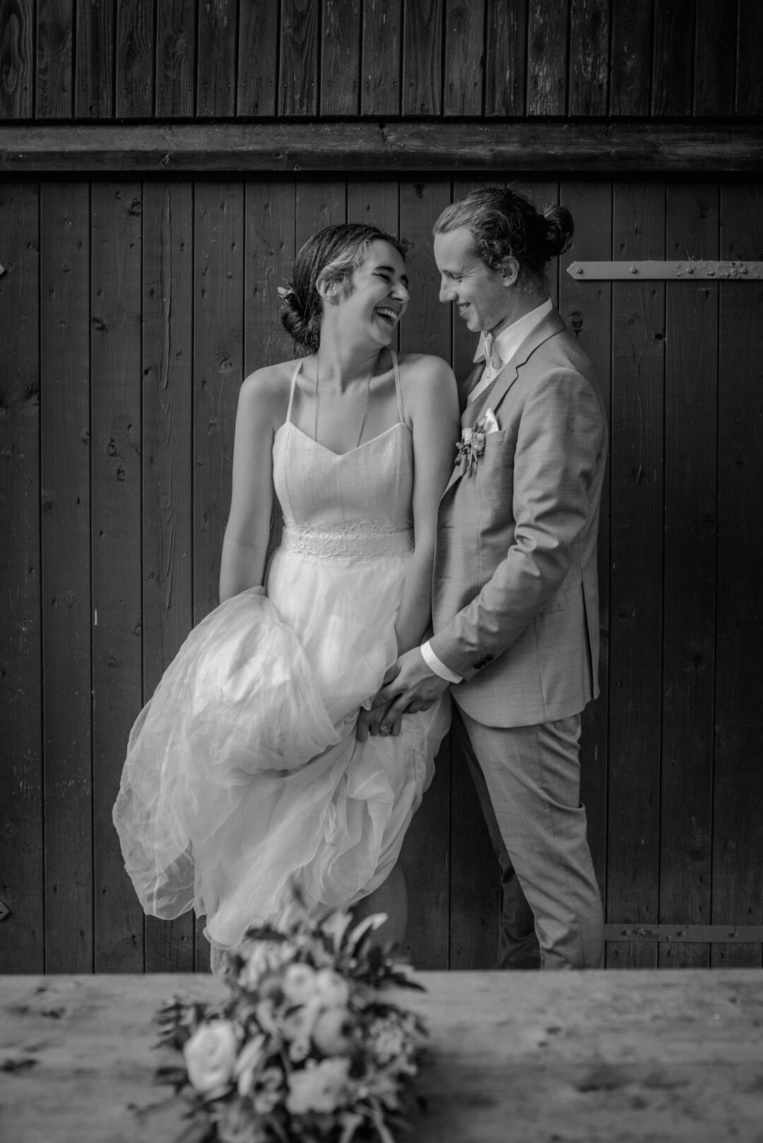 Brautpaar lacht ausgelassen vor Holzwand