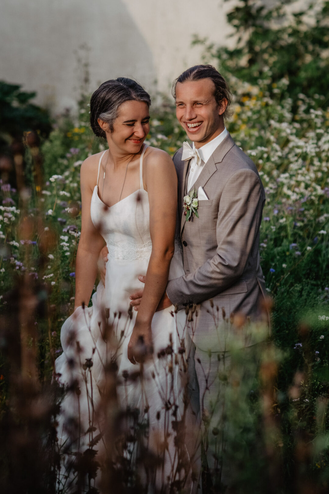 Brautpaar lacht verliebt im wilden Blumenfeld