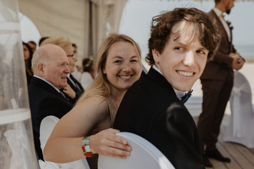 Die Braut sitzt lachend mit einem Hochzeitsgast