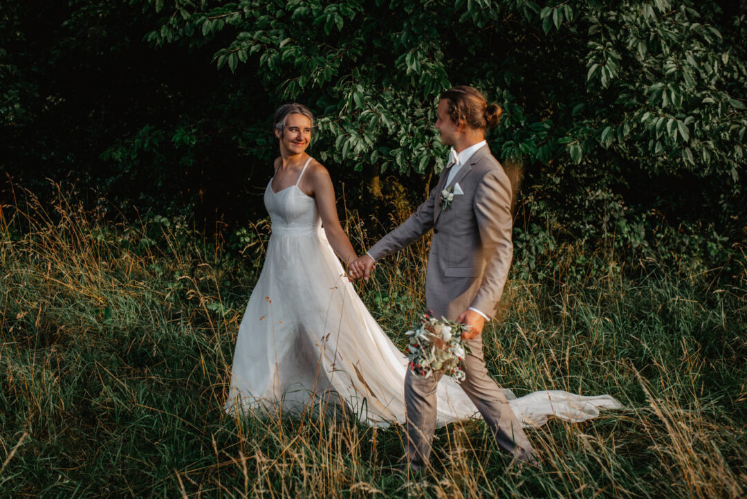 Brautpaar läuft Hand in Hand durch Wiesenweg