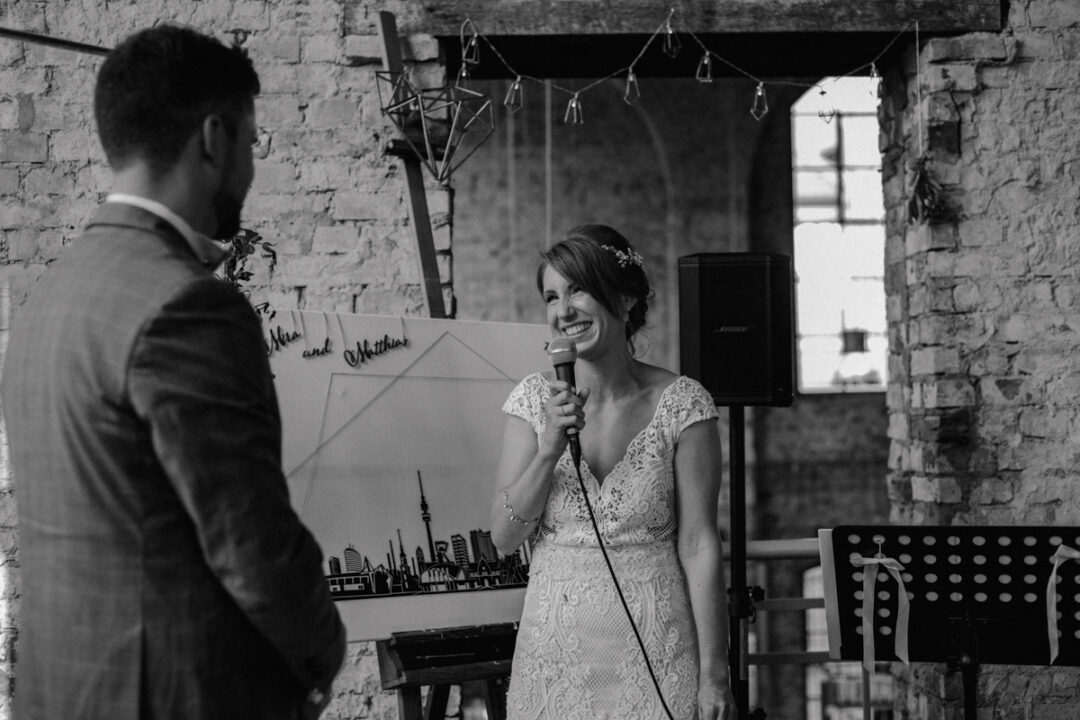 Braut spricht mit Mikrofon vor Industrial-Kulisse während der freien Trauung