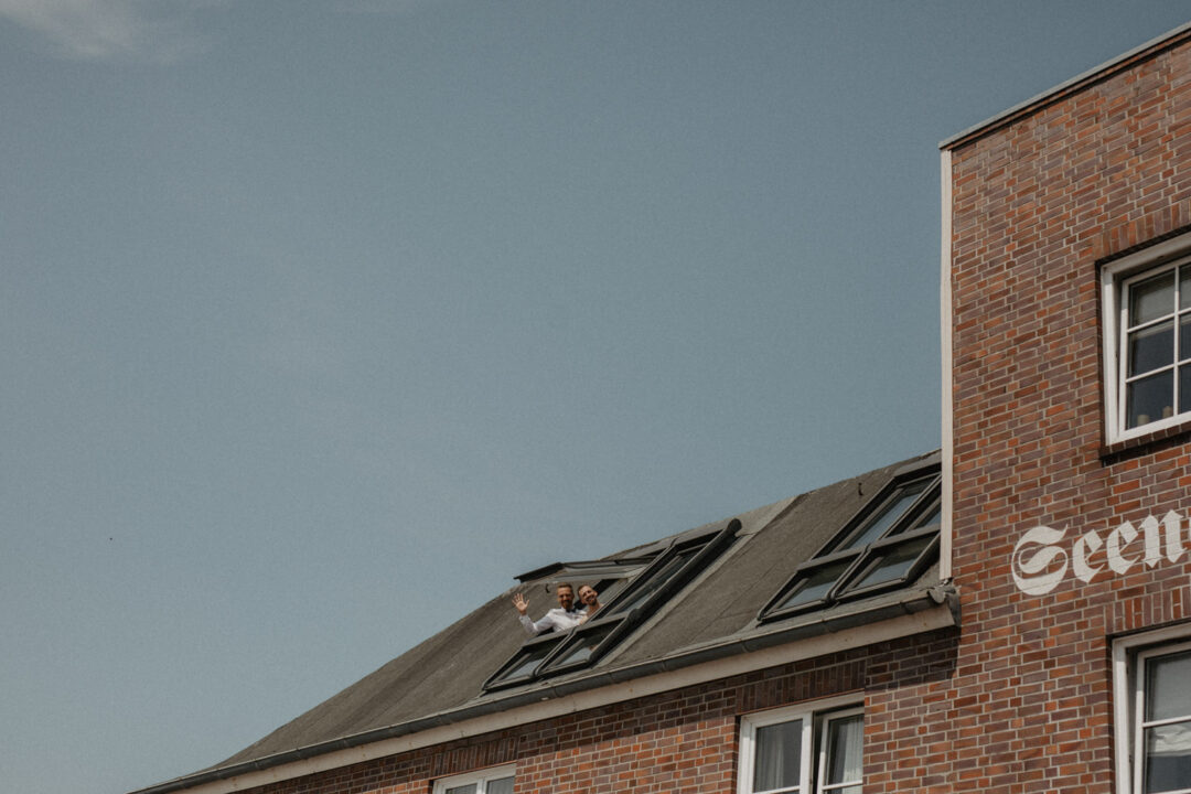Hochzeitspaar winkt aus dem Dachfenster