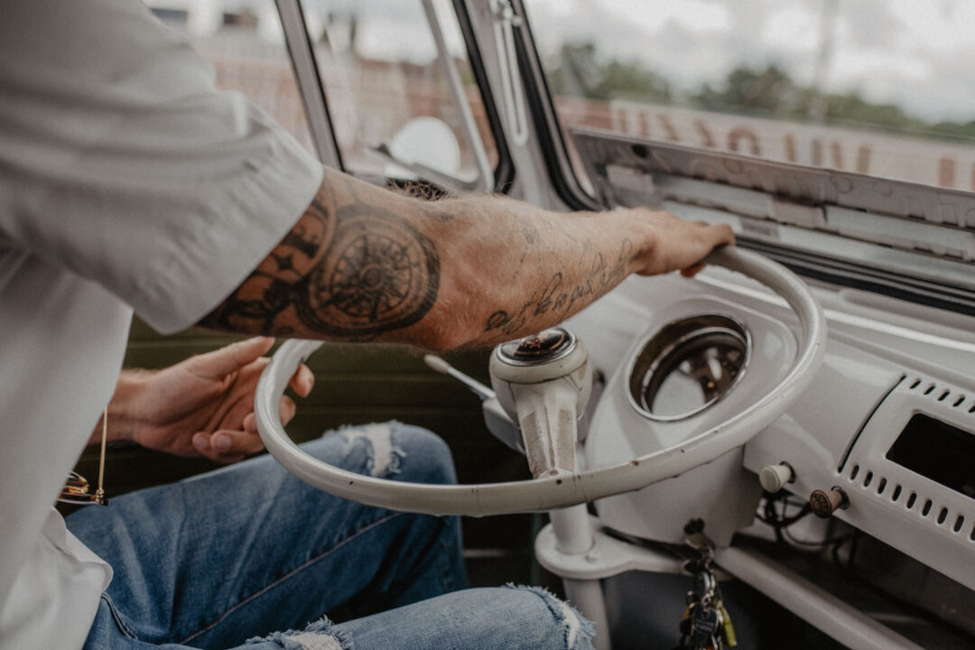 Tattoo-Arm greift ins Lenkrad eines Bullis