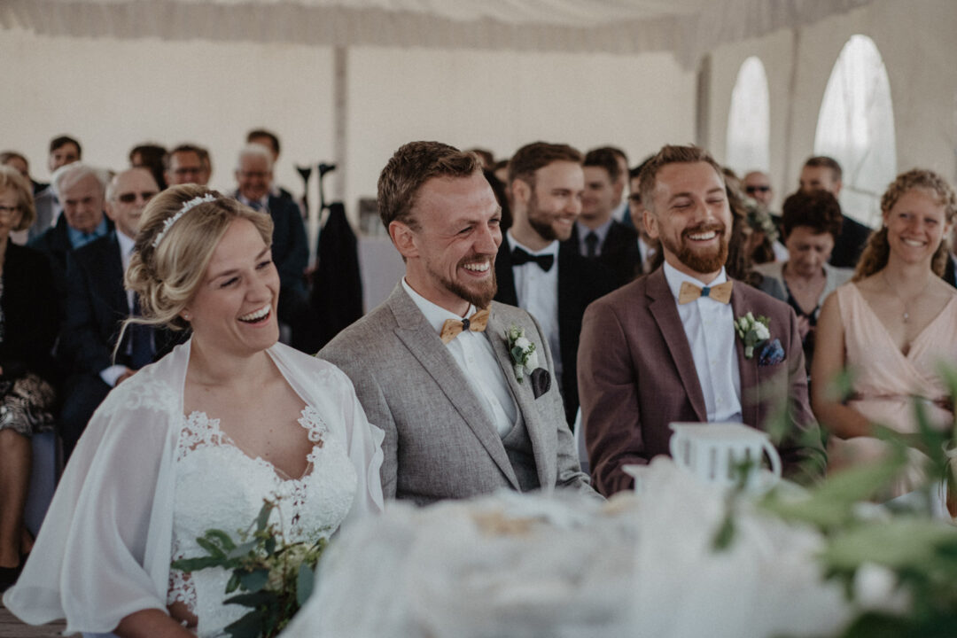 Brautpaar steht lachend mit Trauzeugen und Gaesten