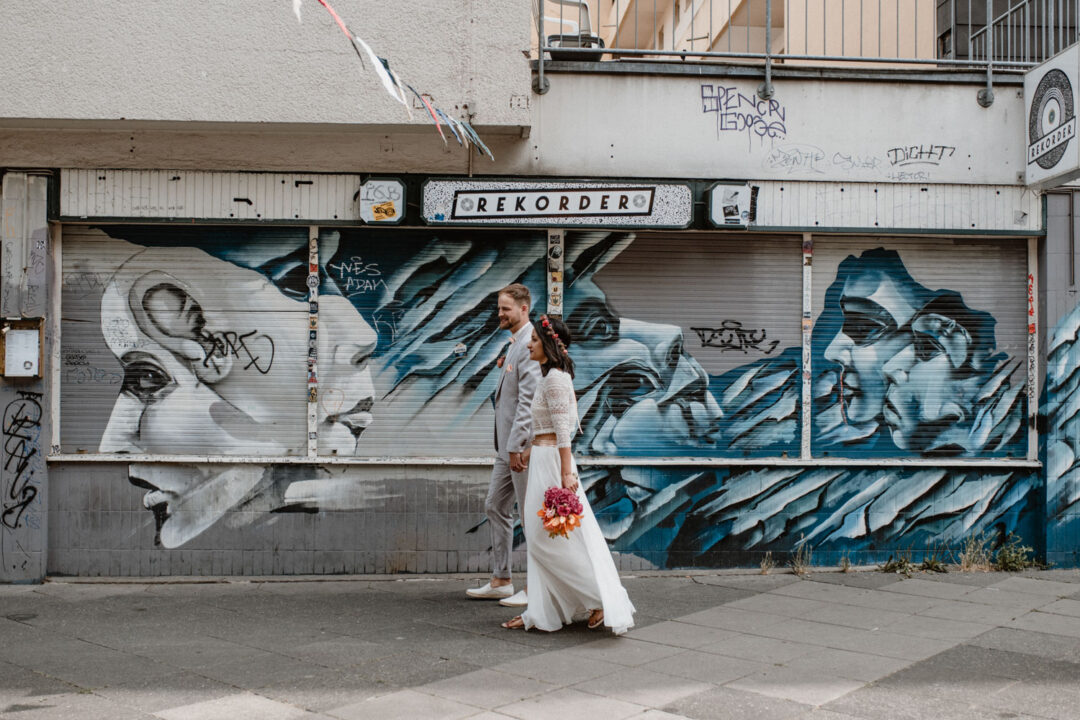 Hochzeitspaar spaziert an Graffitiwand vorbei
