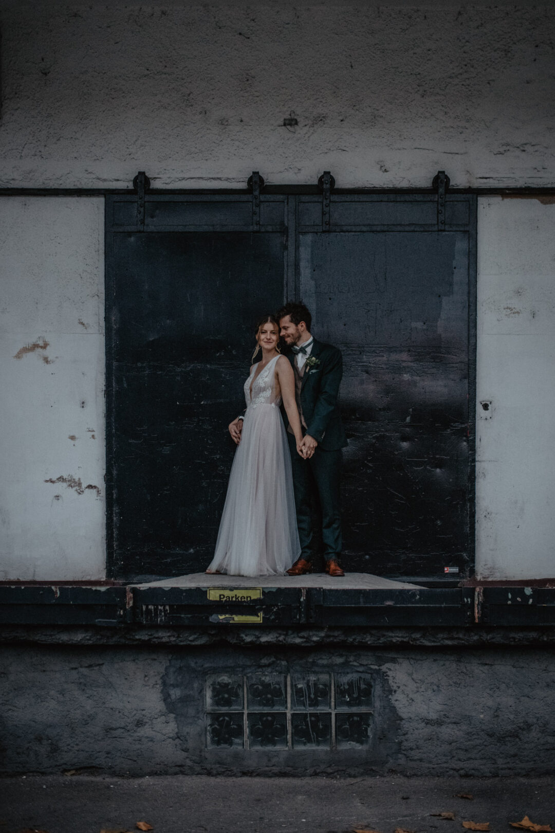 Brautpaar steht eng umschlungen vor altem Industrietor